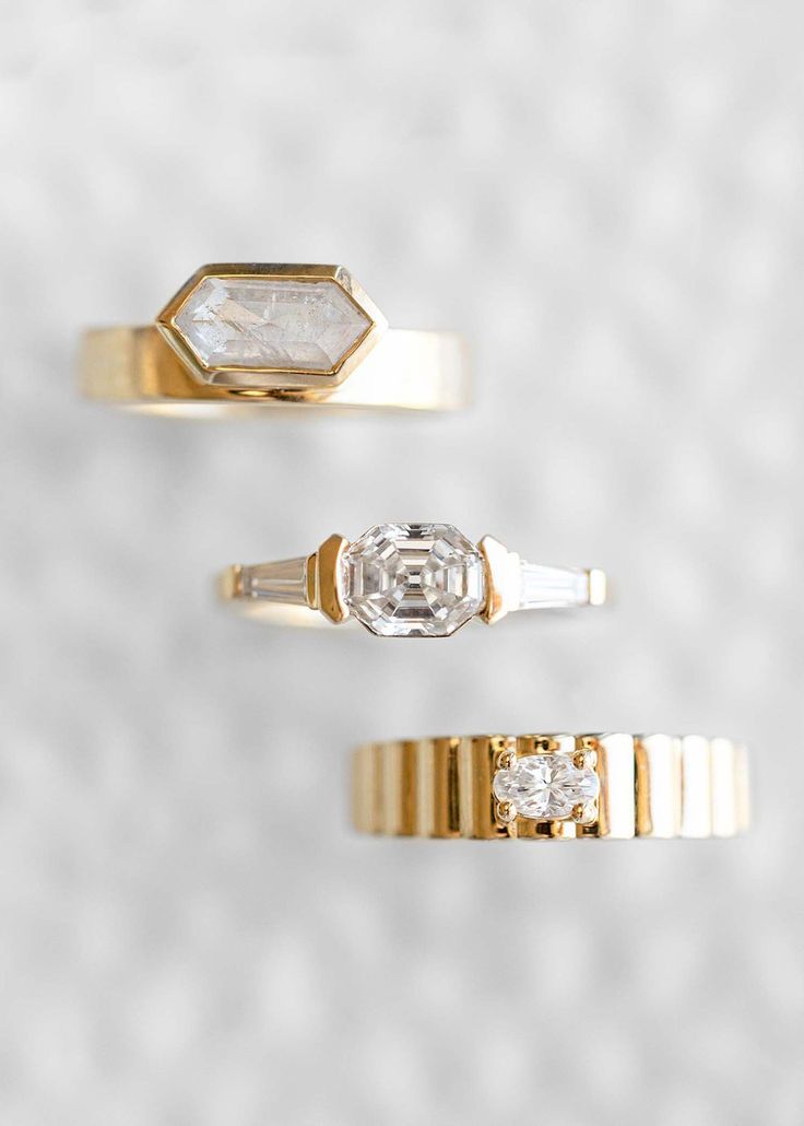 three gold rings with diamonds on them sitting side by side in front of a white background