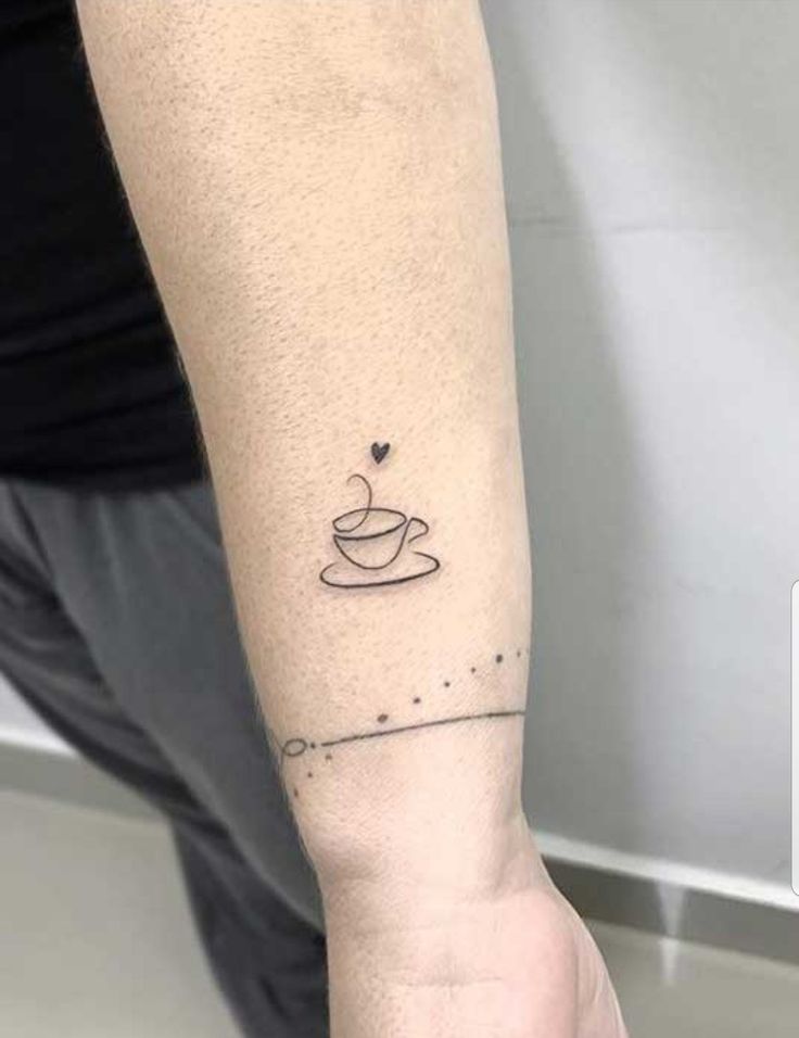 a person with a small tattoo on their arm holding a coffee cup and saucer