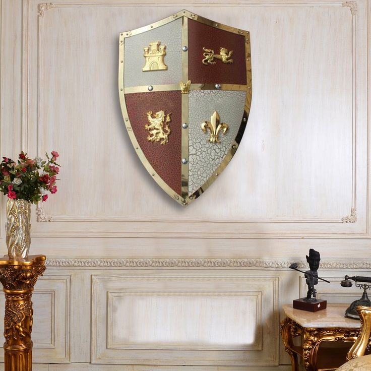 there is a decorative shield on the wall above a table with flowers in vases