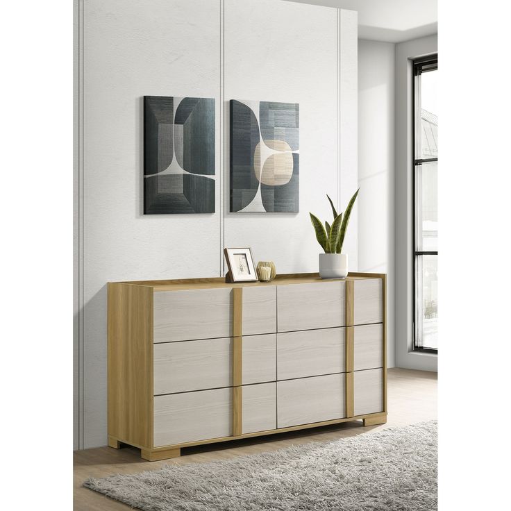 a white and wood dresser with two paintings on it's wall above the drawers