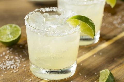 two margaritas sitting on top of a wooden table next to lime slices and salt