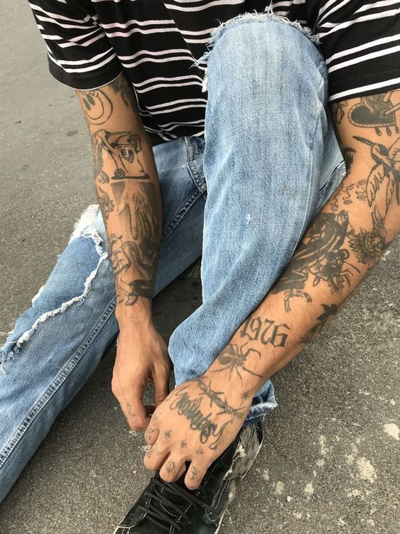 a man sitting on the ground with tattoos on his arms and legs, wearing black shoes