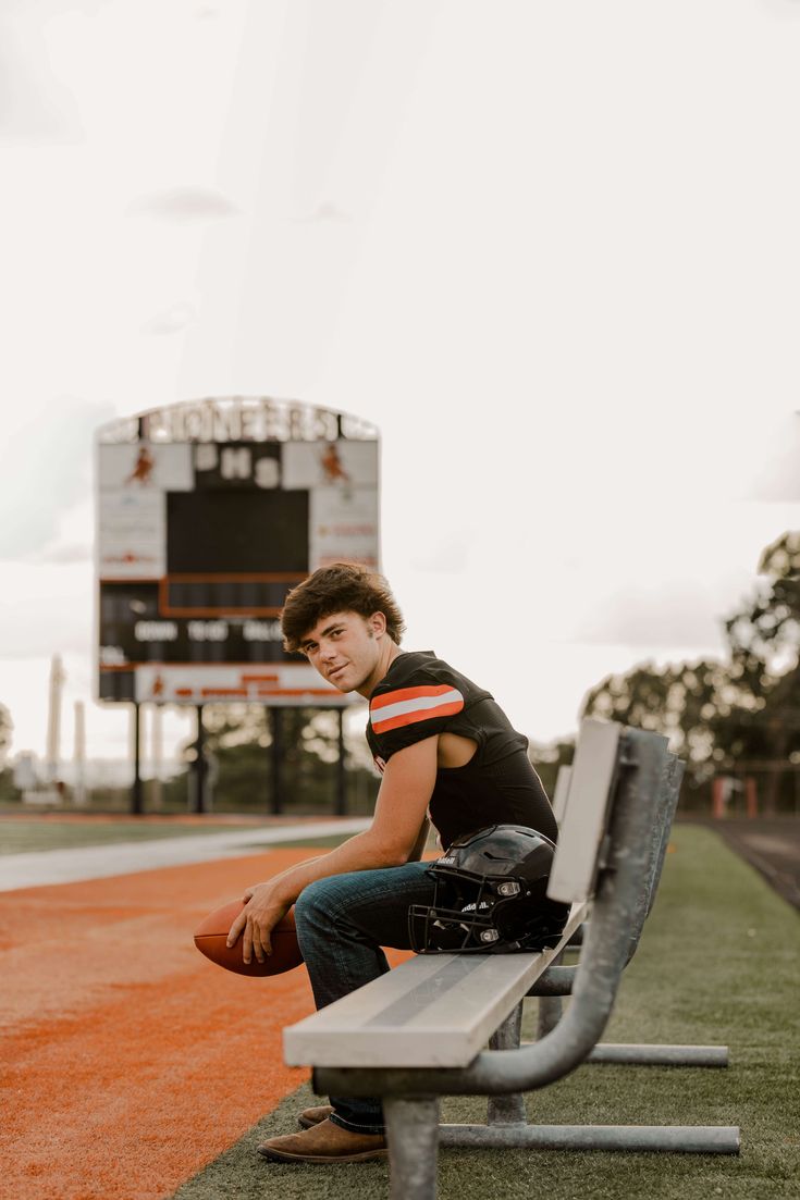 a young man sitting on a bench with a football in his hand and an empty stadium bleacher behind him