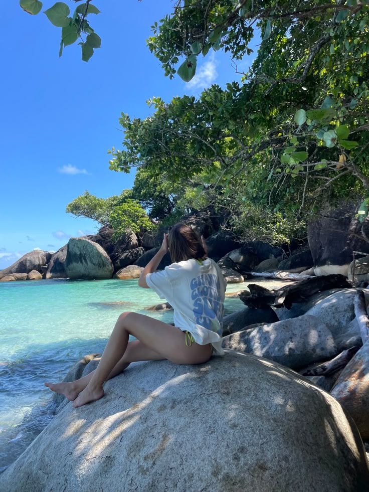 a woman sitting on top of a rock near the ocean