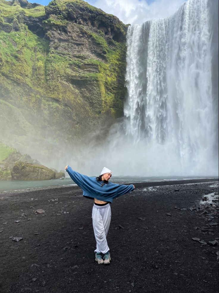 a woman standing in front of a waterfall with her arms spread wide out to the side