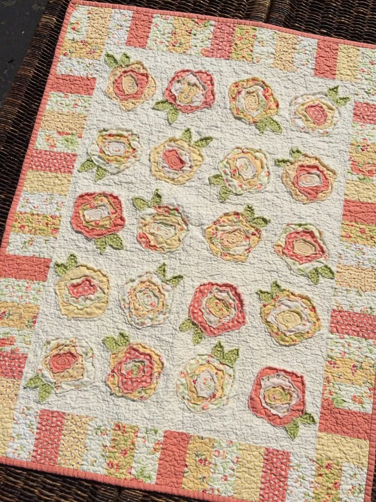 a close up of a quilt on a wooden table with a basket in the background