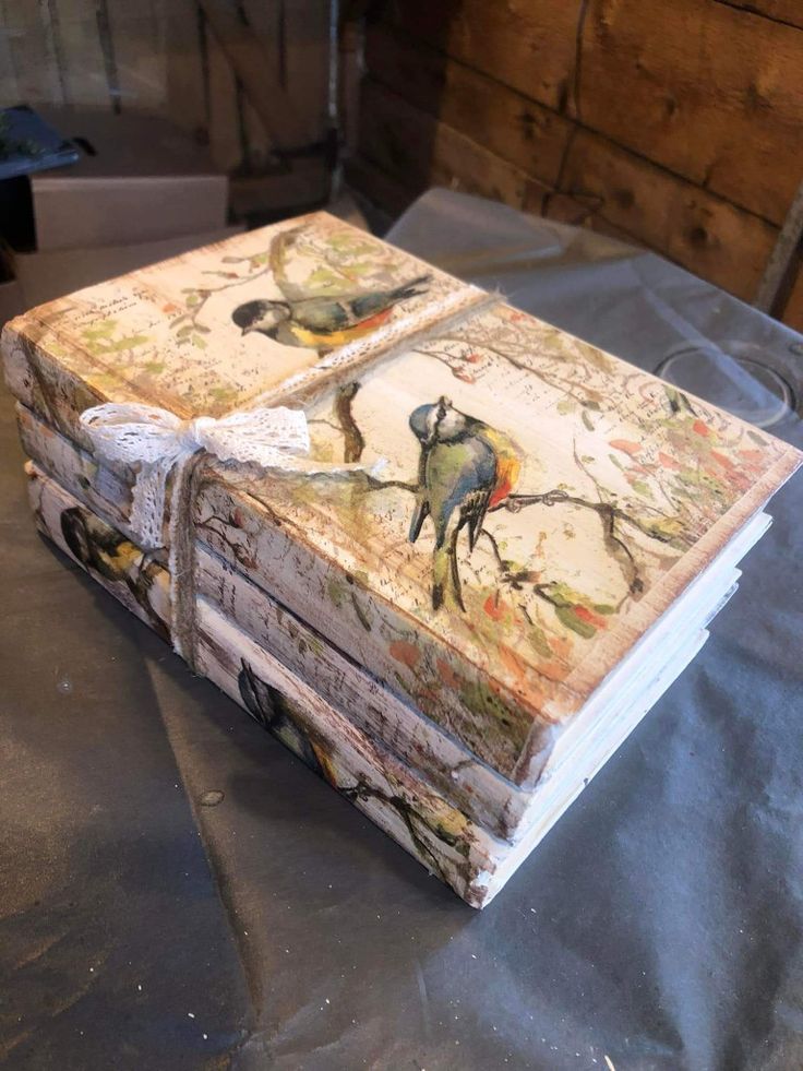 an old book is sitting on top of a table covered in paper and fabric with birds painted on it