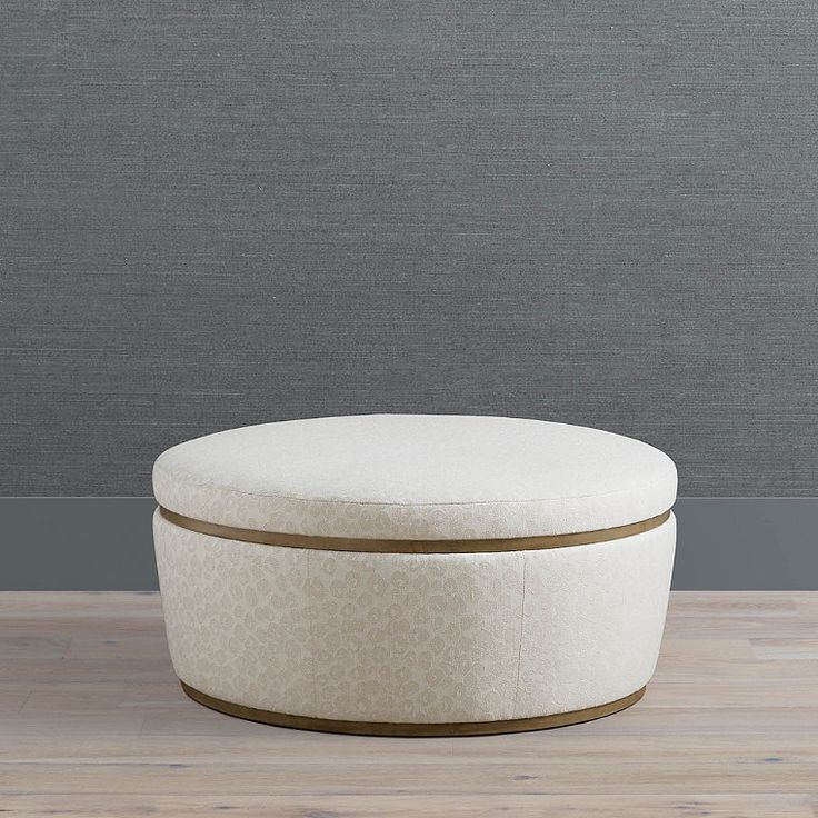 a white round ottoman sitting on top of a wooden floor next to a gray wall