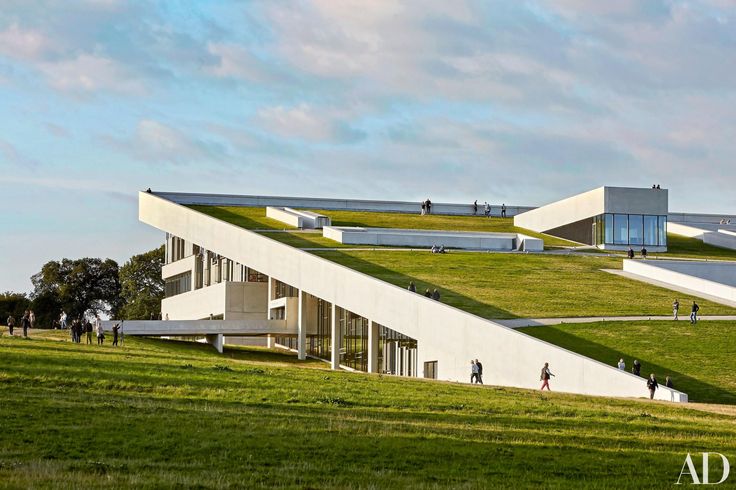 people are walking on the grass covered hill next to a building with green roof and stairs