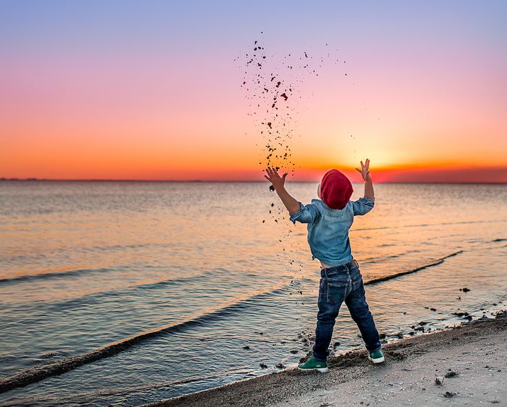 a little boy throwing sand into the air at sunset on the beach with his hands in the air