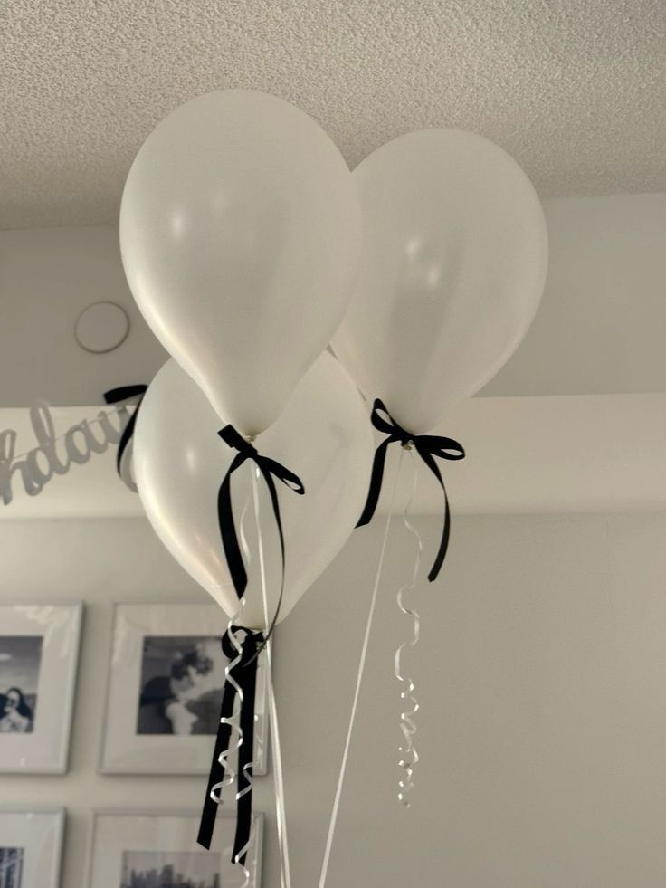 three white balloons with black ribbon tied to them hanging from the ceiling in a room