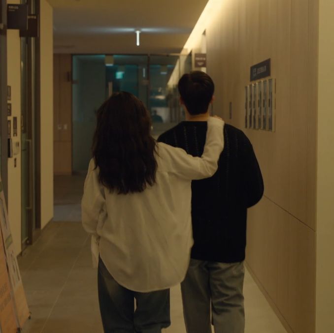 two people walking down a hallway with posters on the wall and doors in the background