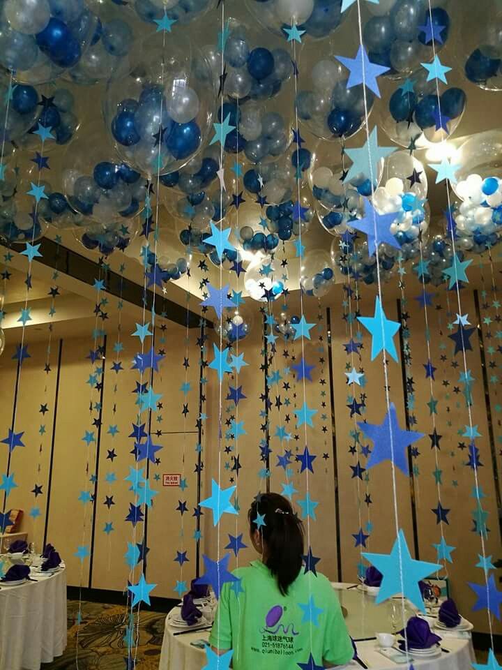 a woman sitting at a table under blue and white stars hanging from the ceiling with balloons