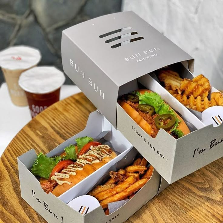 two boxes filled with different types of food sitting on top of a wooden table next to drinks