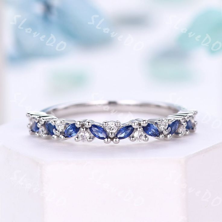 a white gold ring with blue sapphires and diamonds on the side, sitting on a table