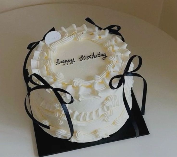 a birthday cake with white frosting and black ribbon