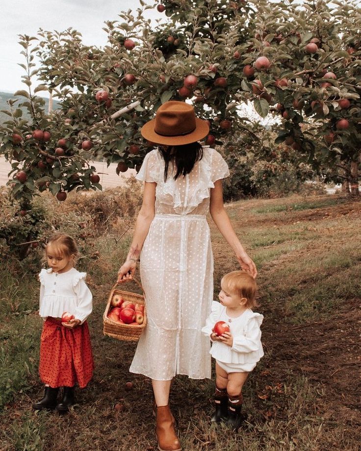 a woman and two children standing in front of an apple tree