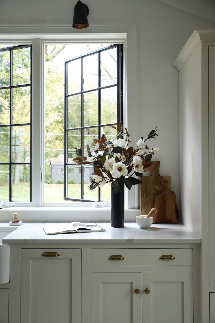 a vase with white flowers sitting on top of a kitchen counter next to a window