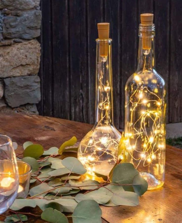 two bottles with fairy lights in them sitting on a table next to glasses and plates