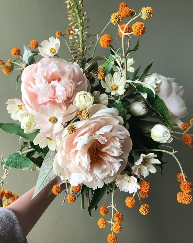 a bouquet of flowers is being held up by someone's hand in front of a gray wall