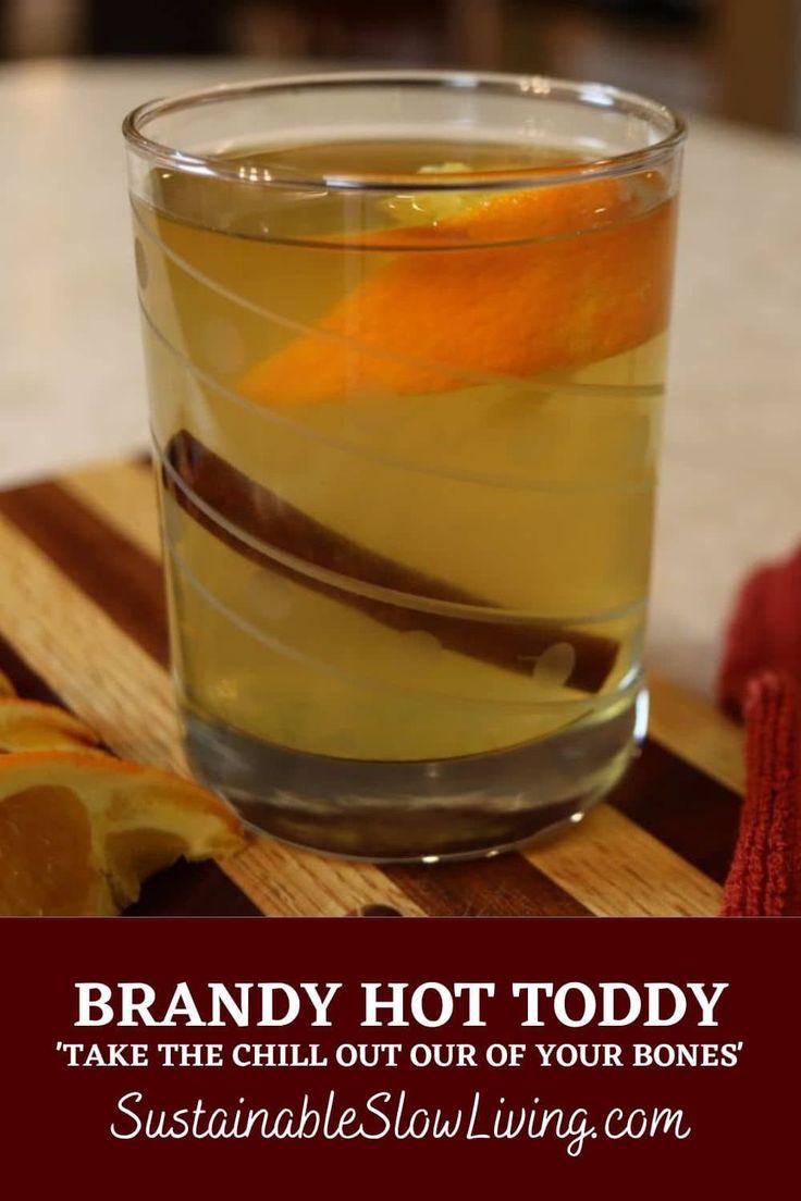 a glass filled with liquid sitting on top of a wooden cutting board next to an orange slice