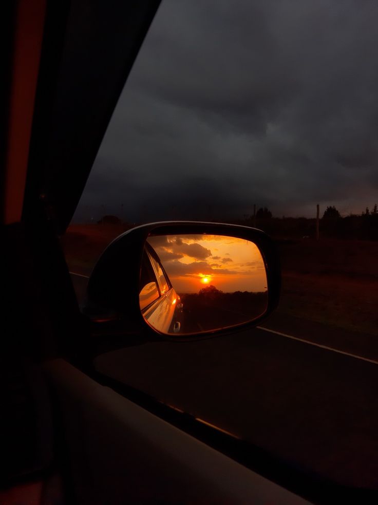 the sun is setting in the distance as seen from a car's side mirror