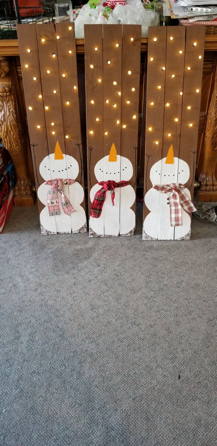 two snowmen standing next to each other in front of a wooden sign with lights