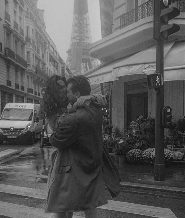 a man and woman kissing in front of the eiffel tower on a rainy day