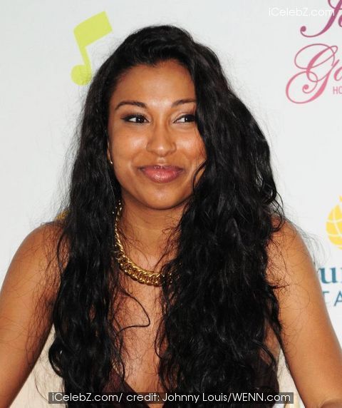 a woman with long black hair wearing a white dress and gold necklace smiling at the camera