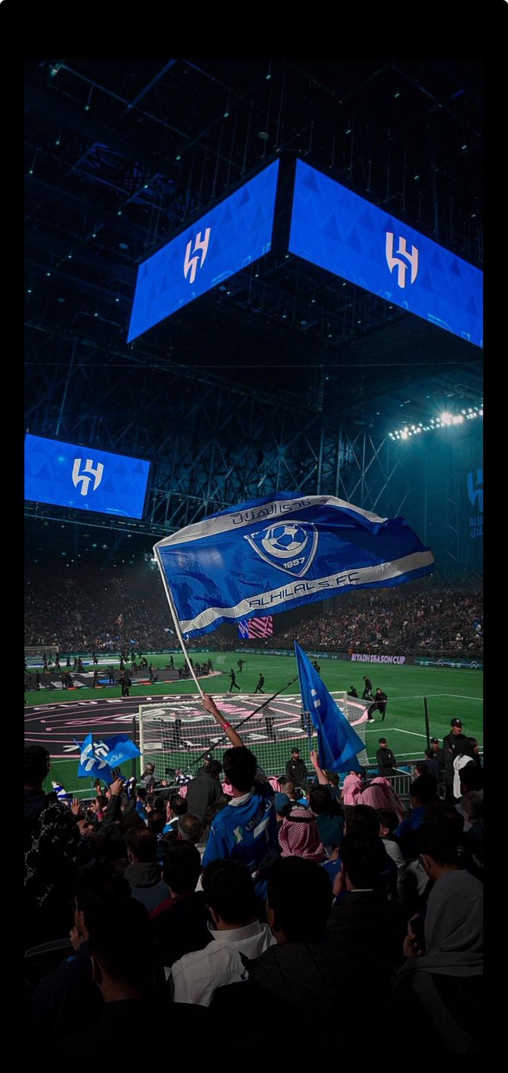 a group of people standing on top of a soccer field holding up blue and white flags