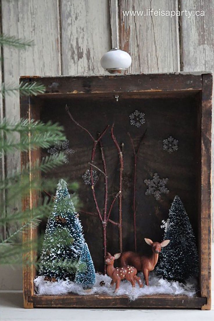 a small wooden box with some deer and trees in the snow next to a pine tree