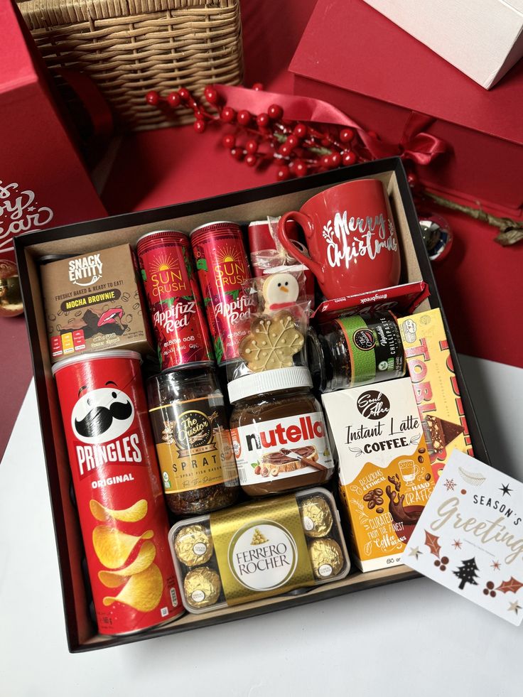 a gift box filled with assorted snacks and coffees next to a christmas tree