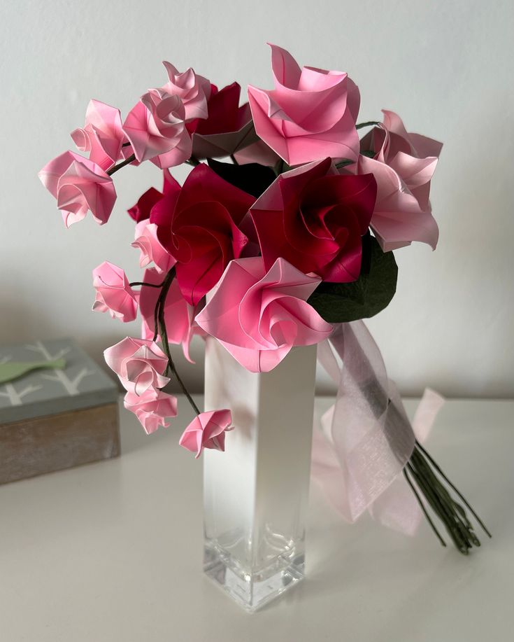 a vase filled with pink and red flowers sitting on top of a white table next to a stack of books