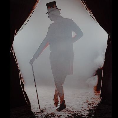 a man with a top hat and cane walking through foggy area in the dark