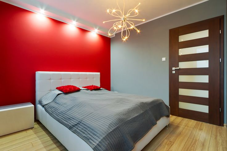 a bedroom with red walls, white bedding and wooden flooring is pictured in this image