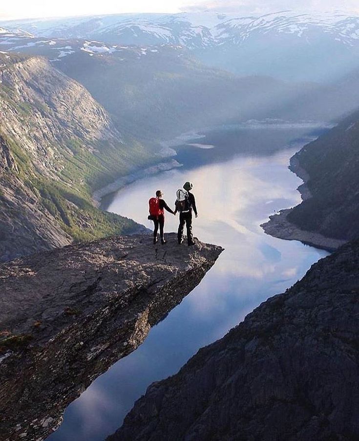 two people holding hands while standing on top of a cliff overlooking a body of water