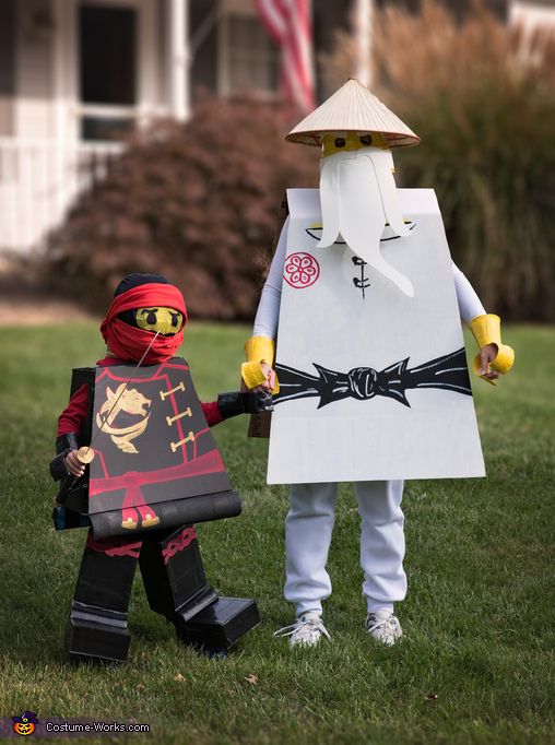 two children dressed up in legos standing on the grass with one holding a sign