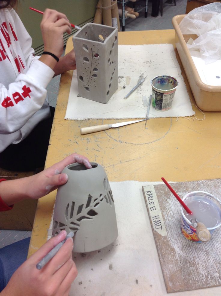 two people sitting at a table making vases with paint and paper on the table