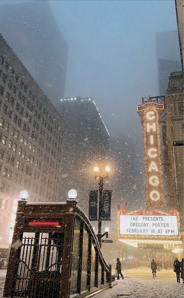 people are walking in the snow near theater marquee and traffic lights at night