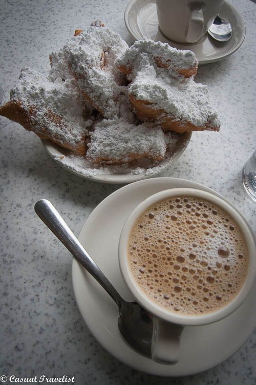 a cup of coffee with powdered sugar on top next to doughnuts and a spoon