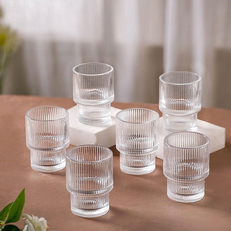 six clear glass tumblers sitting on top of a table next to a vase with flowers in it