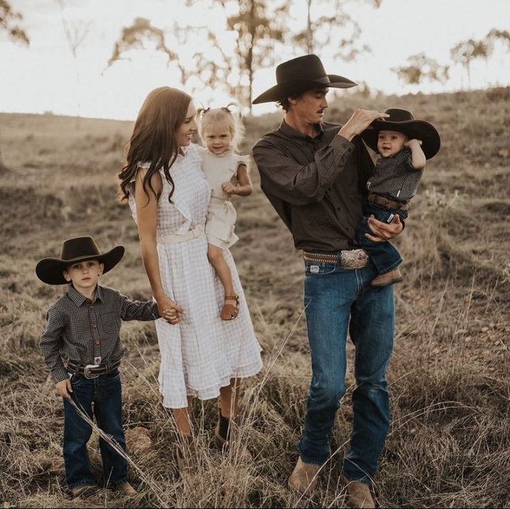 a man, woman and two children are standing in the grass with cowboy hats on