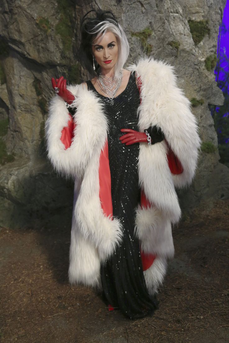 a woman in a black dress and white fur coat standing next to a rock wall