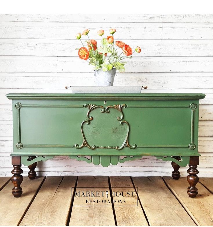 a green dresser sitting on top of a wooden floor next to a vase with flowers