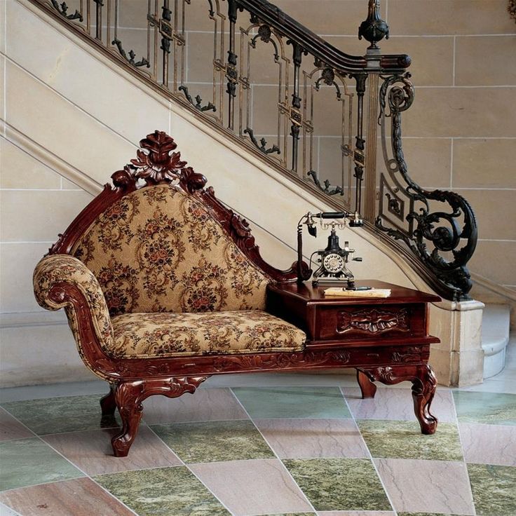 an ornately decorated chair sitting in front of a stair case next to a table with a clock on it