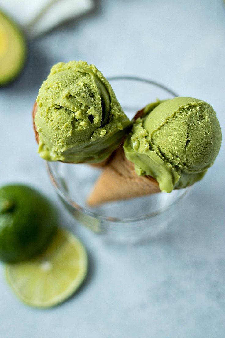 two scoops of green ice cream in a glass with lime slices on the side