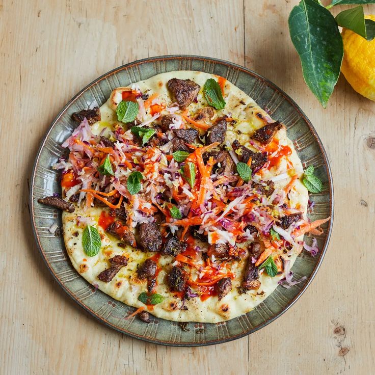 a pizza with meat, cheese and vegetables on a plate next to a lemon tree