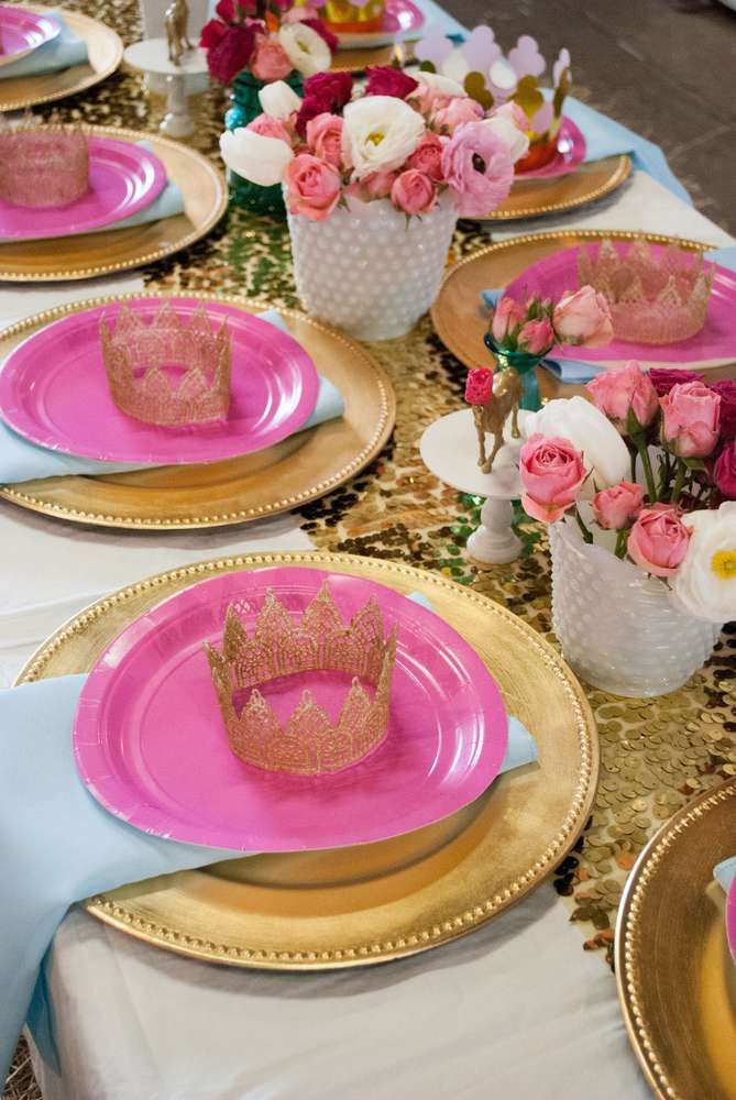 the table is set with pink and gold plates, napkins, and flower centerpieces