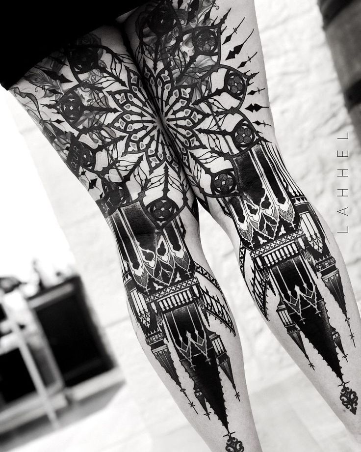 black and white photograph of legs with tattoos on them that have clock faces, trees, and stars