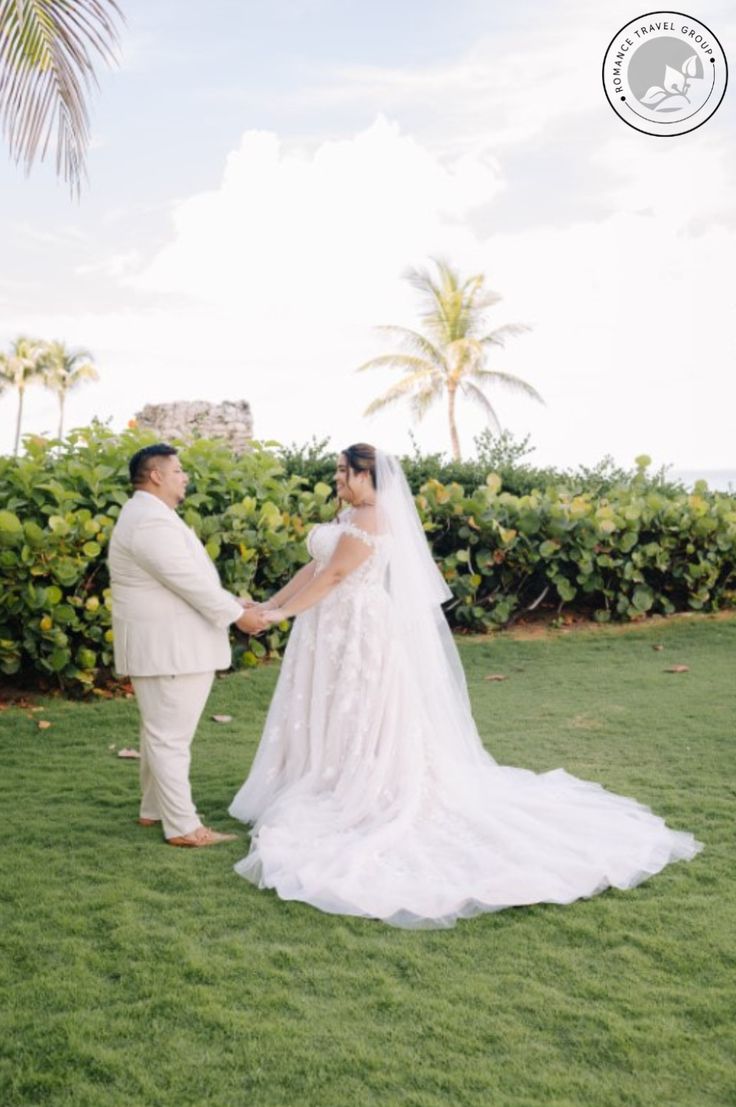 a bride and groom standing in the grass at their wedding ceremony with palm trees behind them